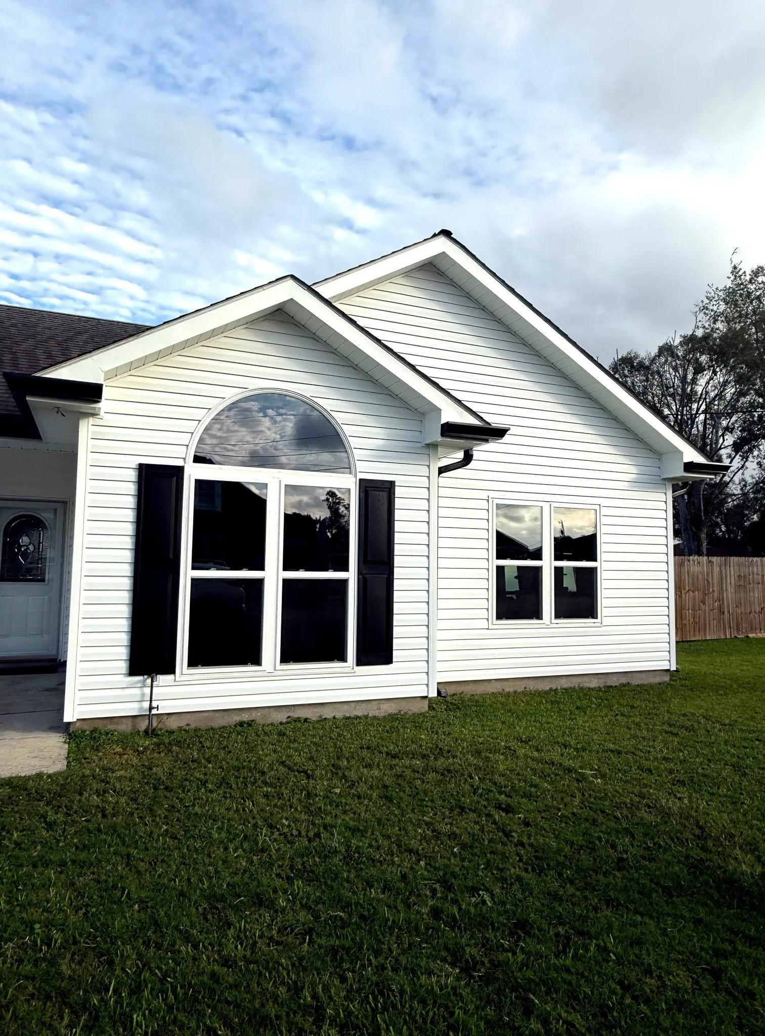 Newly installed white vinyl siding on a modern home, featuring black shutters and large windows, showcasing enhanced curb appeal and durability.