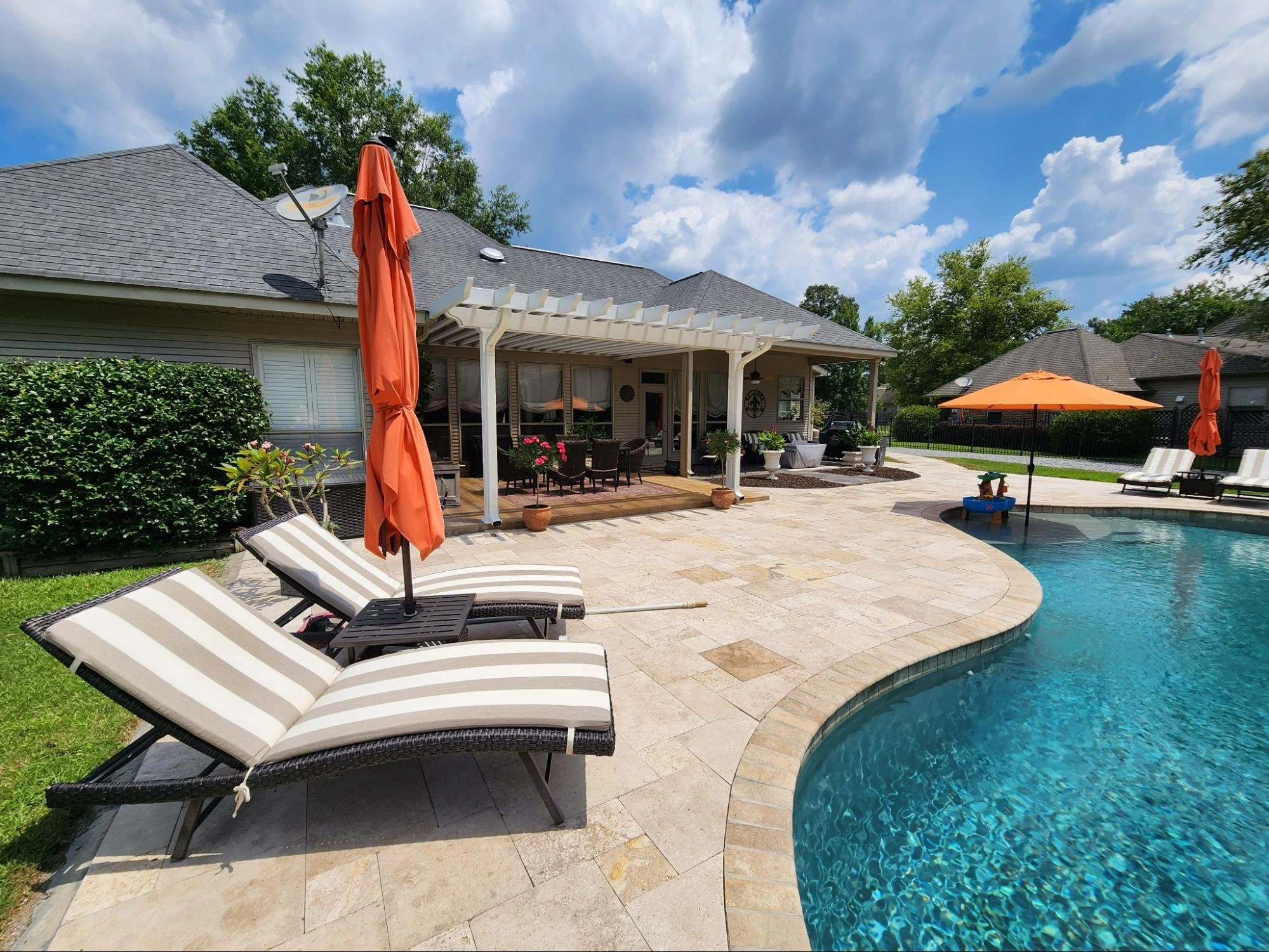 Outdoor pool area with lounge chairs, orange umbrellas, and a well-maintained garden, showcasing a residential home in New Orleans, ideal for exterior home improvement projects.