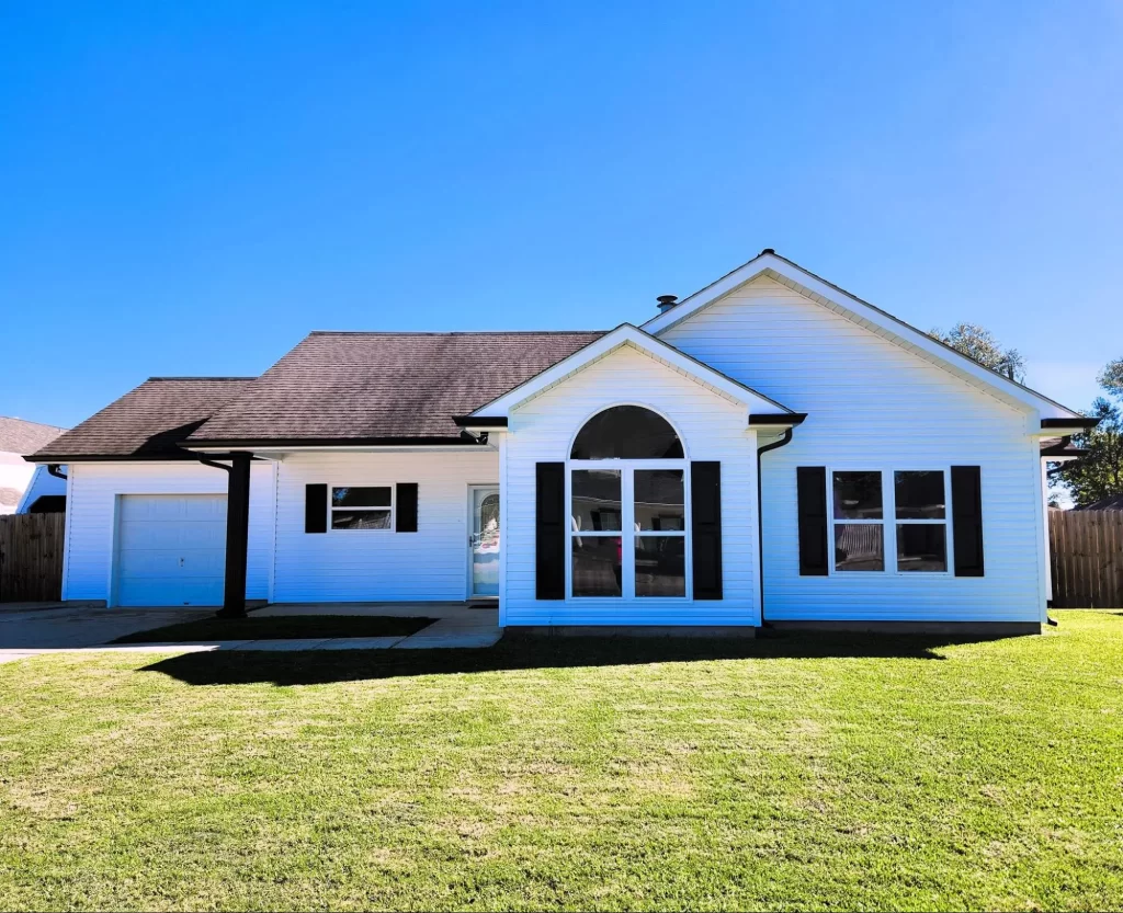 White house with black shutters and a garage, showcasing popular siding options for homes in Metairie and New Orleans, set against a clear blue sky and green lawn.