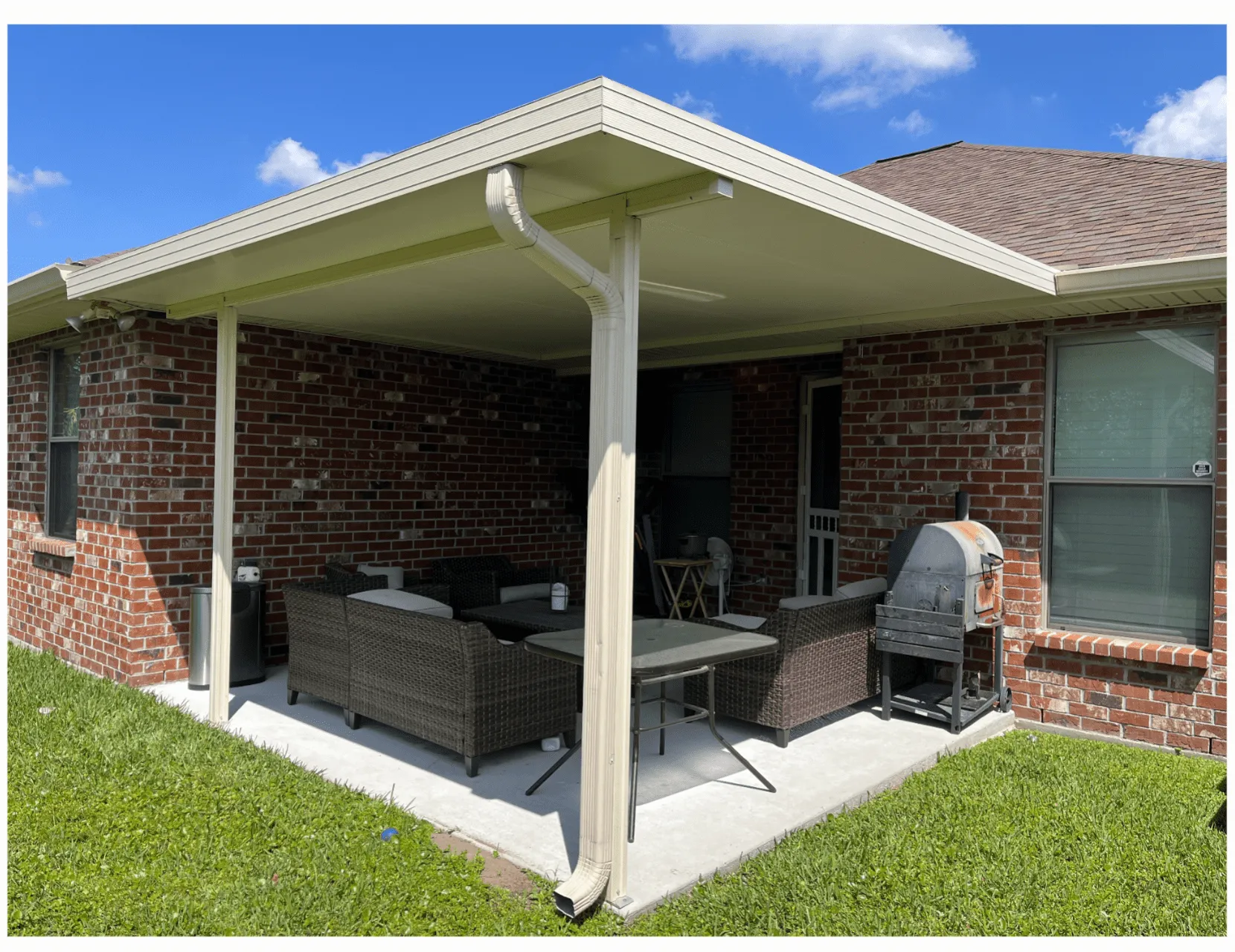 Patio cover featuring insulated roof panels with a seating area, table, and grill, enhancing outdoor living space and providing shade and protection from weather.