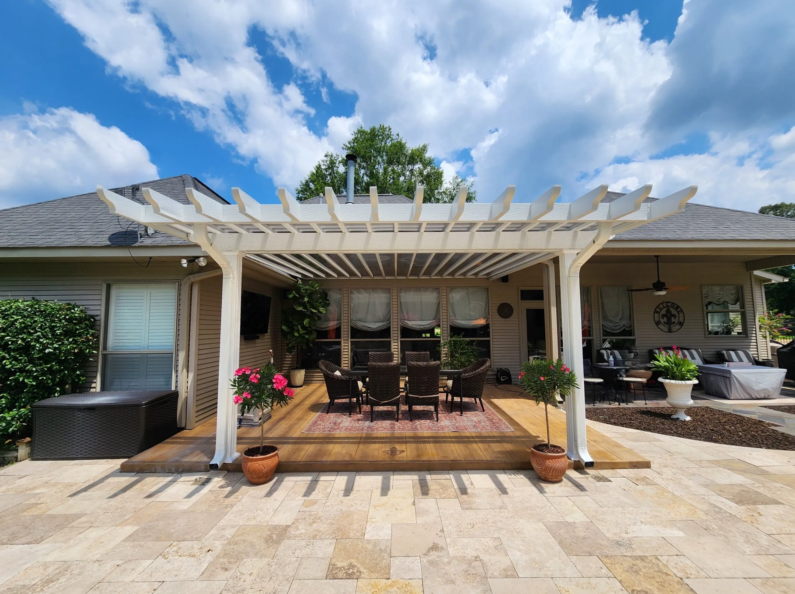 Patio cover featuring a white pergola with insulated roof panels, surrounded by outdoor seating, flowering plants, and a stone patio, enhancing outdoor living space.