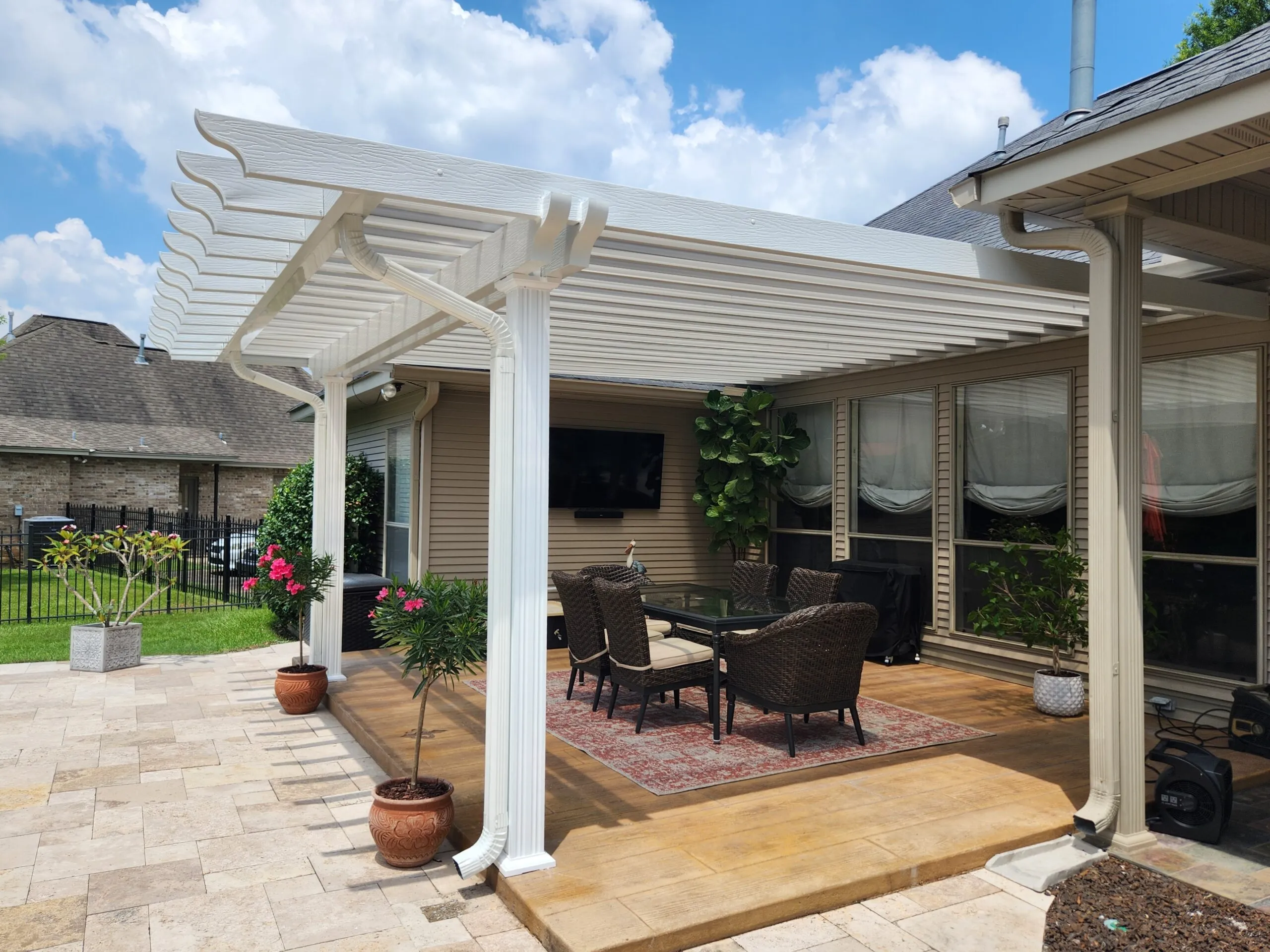 Patio cover featuring insulated roof panels and elegant lattice design, surrounded by potted plants and outdoor furniture on a stone patio, enhancing outdoor living space.