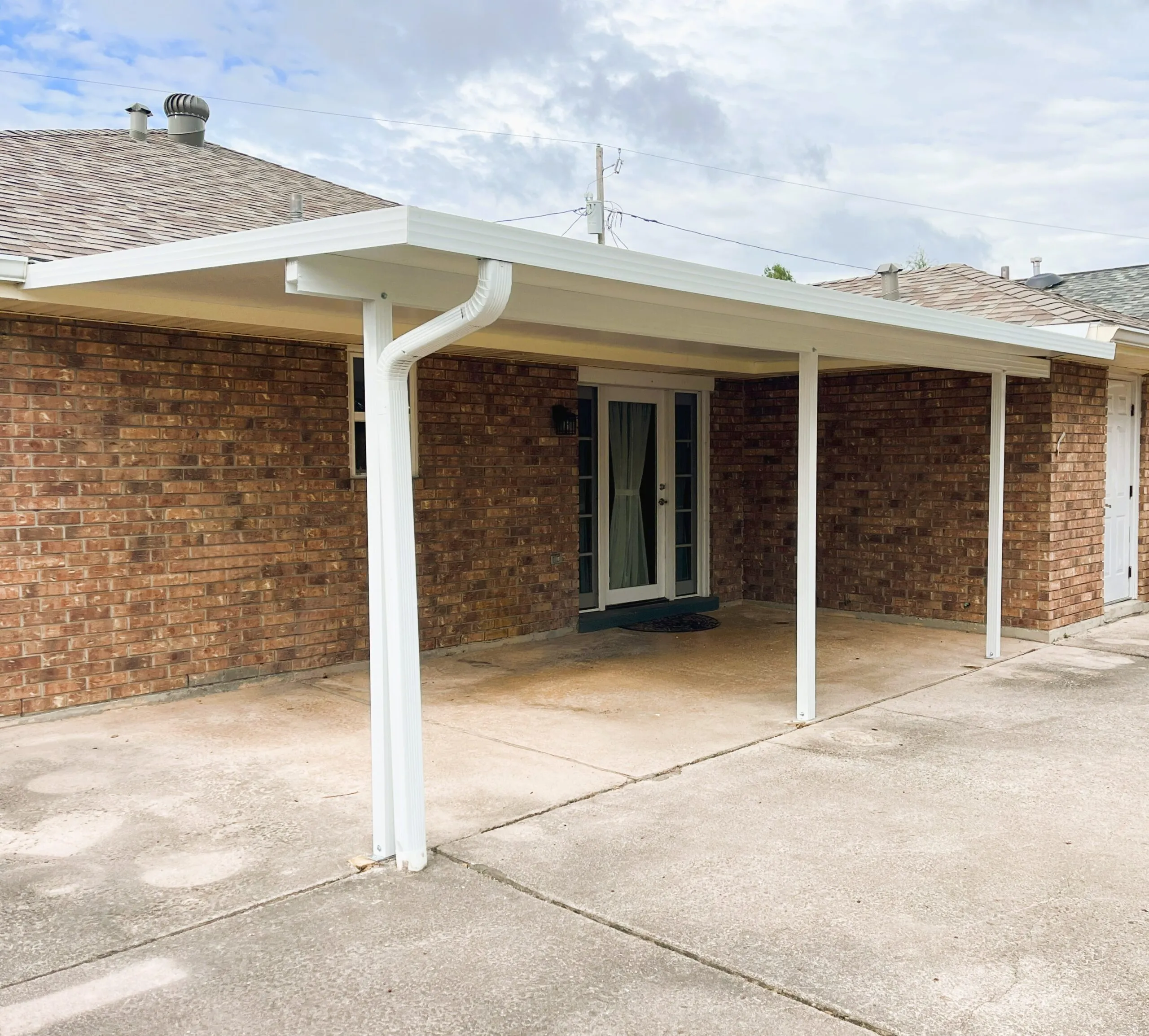 Insulated patio cover with a flat roof design attached to a brick home, providing shade and weather protection for outdoor living spaces.