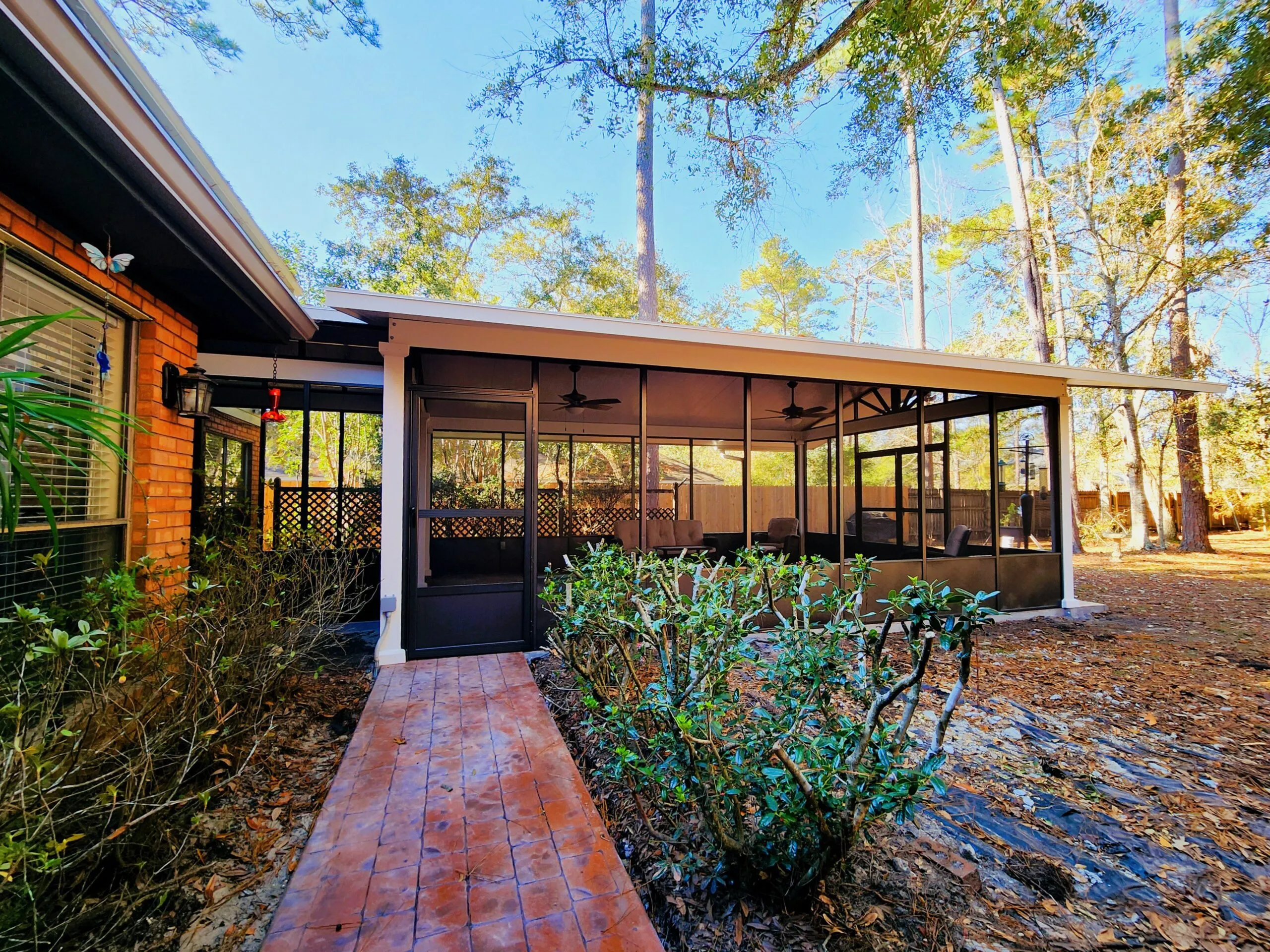 Freestanding bronze screen room with gabled roof, cedar-embossed white patio cover, and terracotta stamped concrete walkway in Slidell, Louisiana.