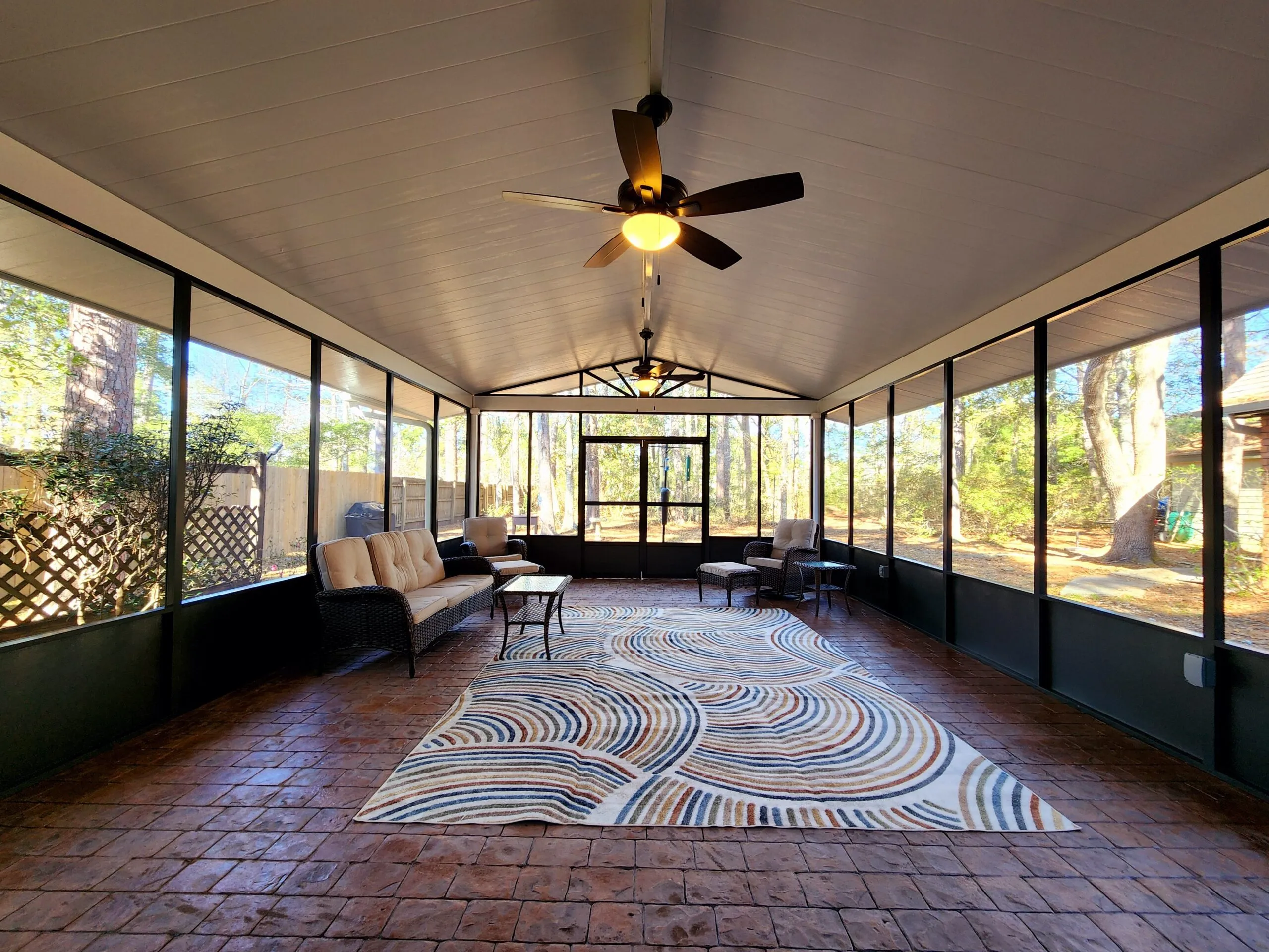Freestanding bronze screen room in Slidell, LA, featuring a cedar-embossed white insulated patio cover, gabled roof, terracotta stamped concrete flooring, and stylish furnishings.