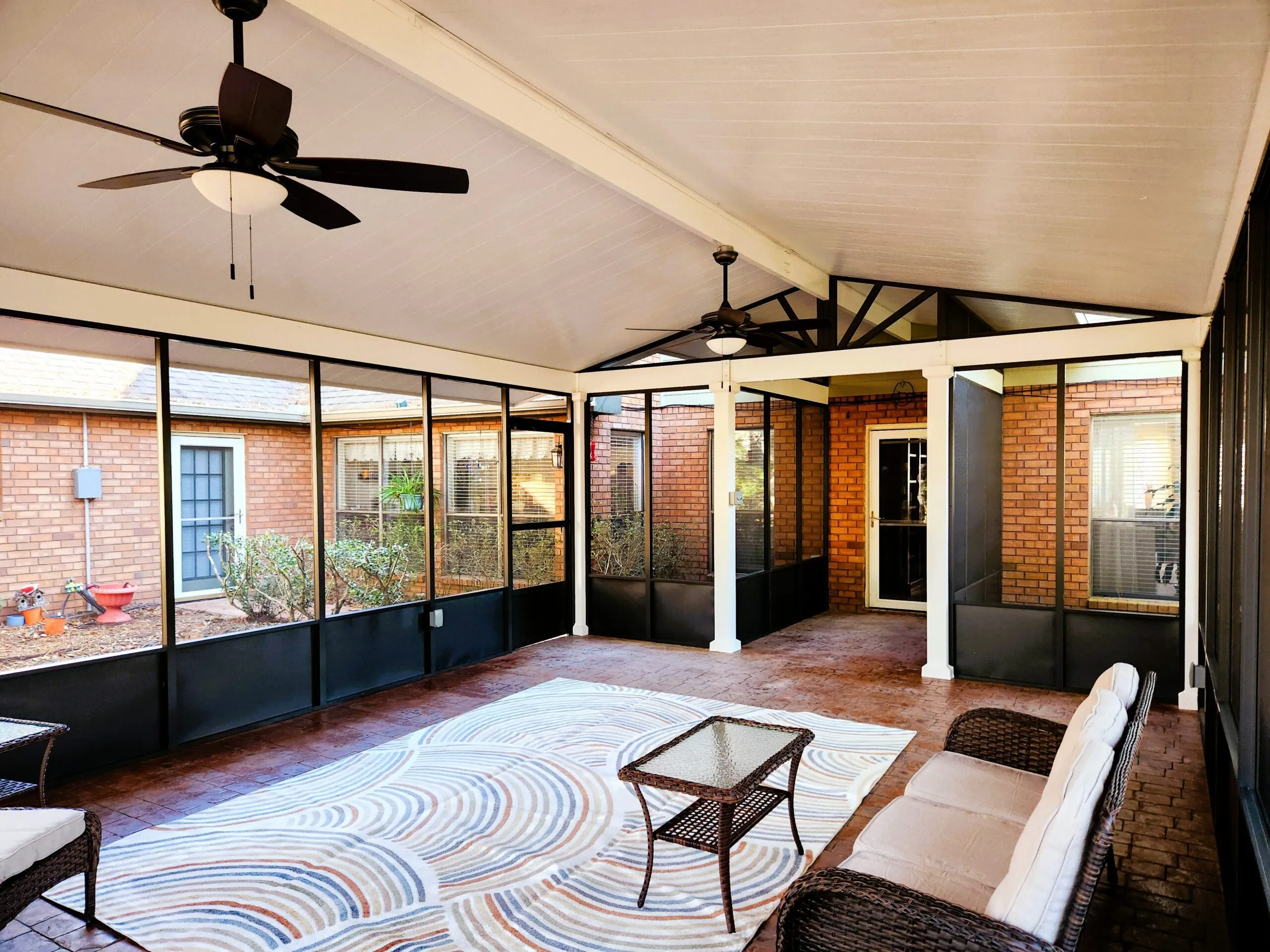 Freestanding bronze screen room with gabled roof, cedar-embossed white patio cover, terracotta stamped concrete flooring, and modern furnishings in Slidell, LA outdoor space renovation.