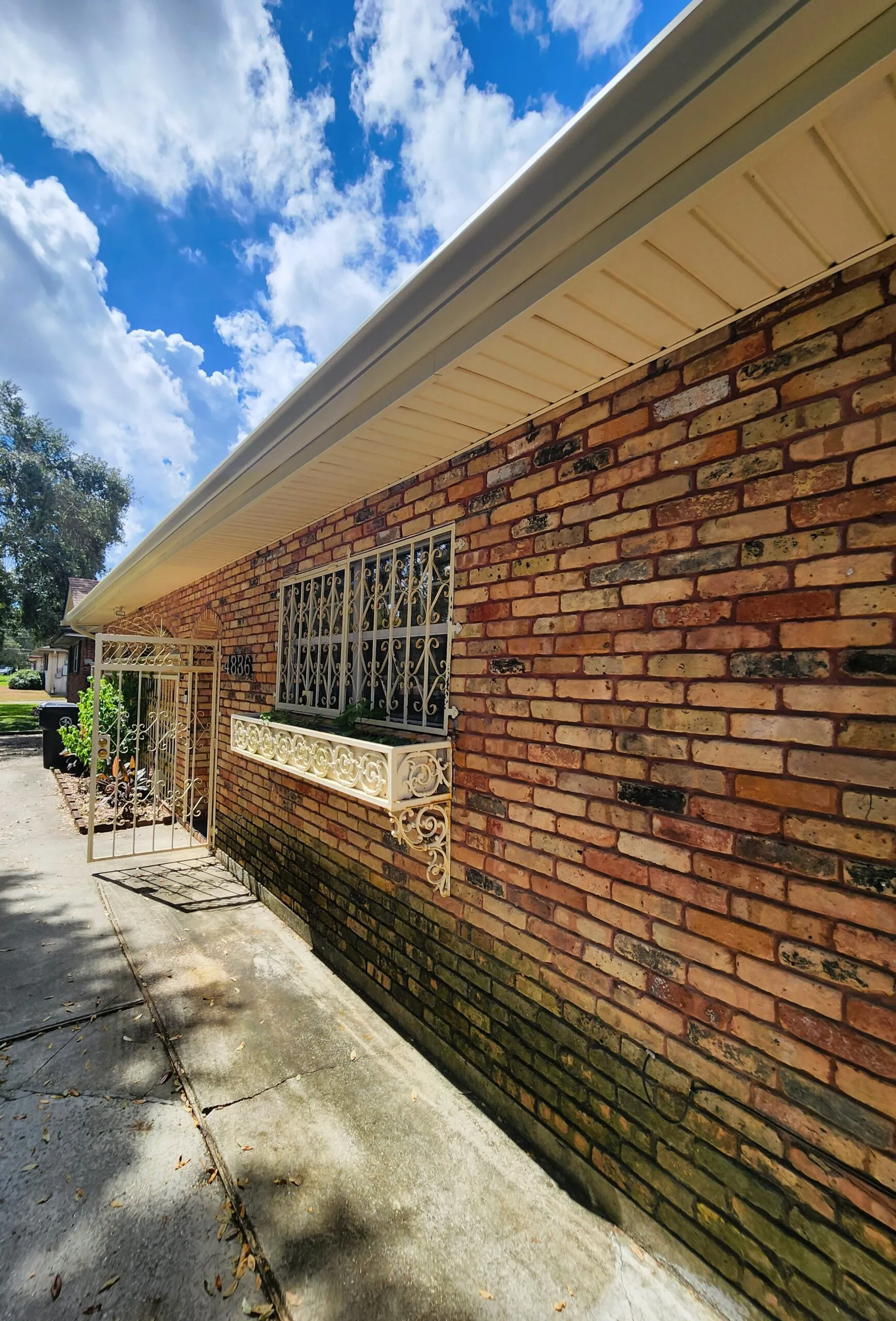 Seamless aluminum gutter installed on a residential brick home, showcasing professional craftsmanship and water diversion capabilities under a clear blue sky.