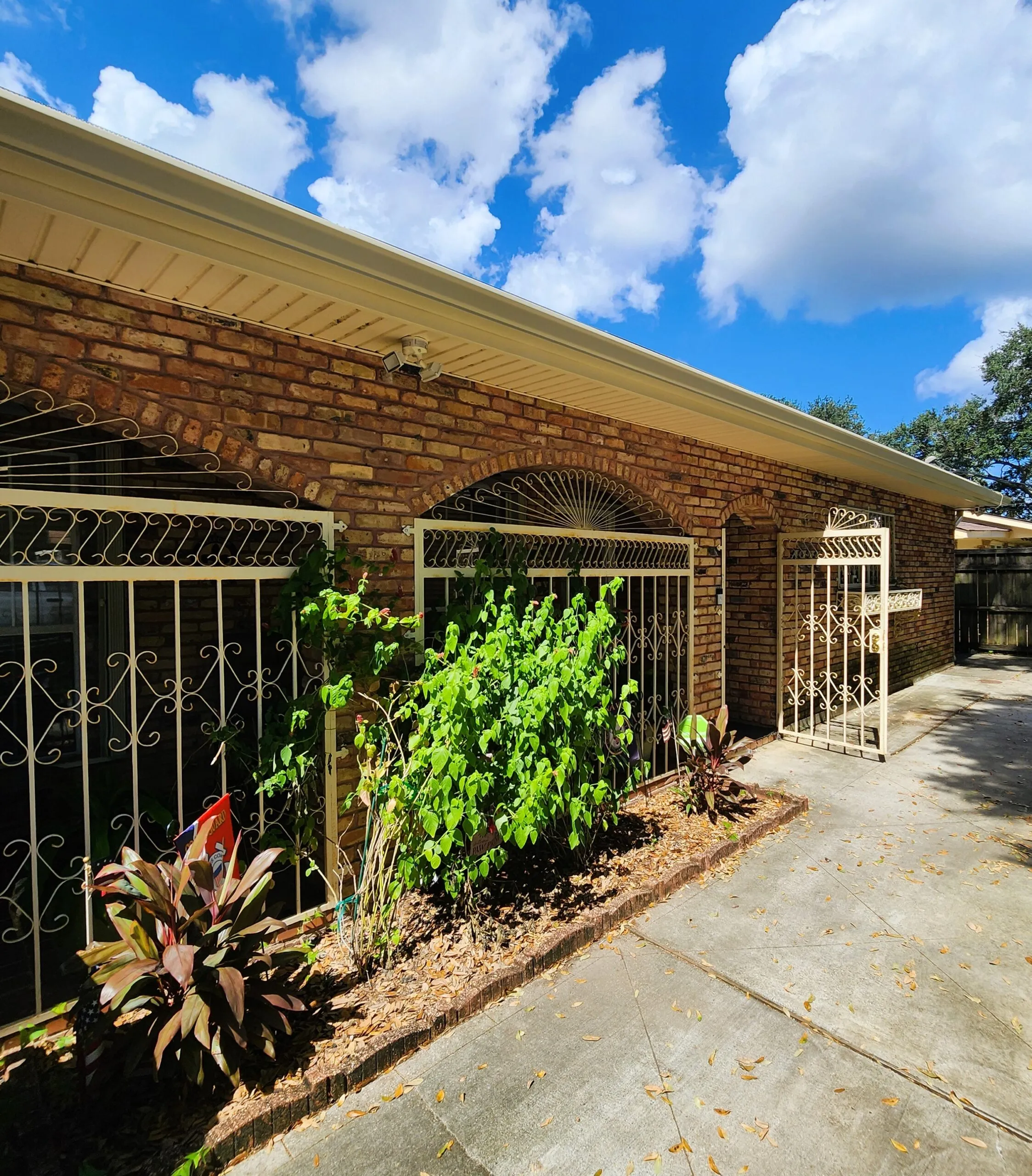 Seamless aluminum gutters installed on a brick home, surrounded by greenery and decorative fencing, showcasing professional exterior home improvement.