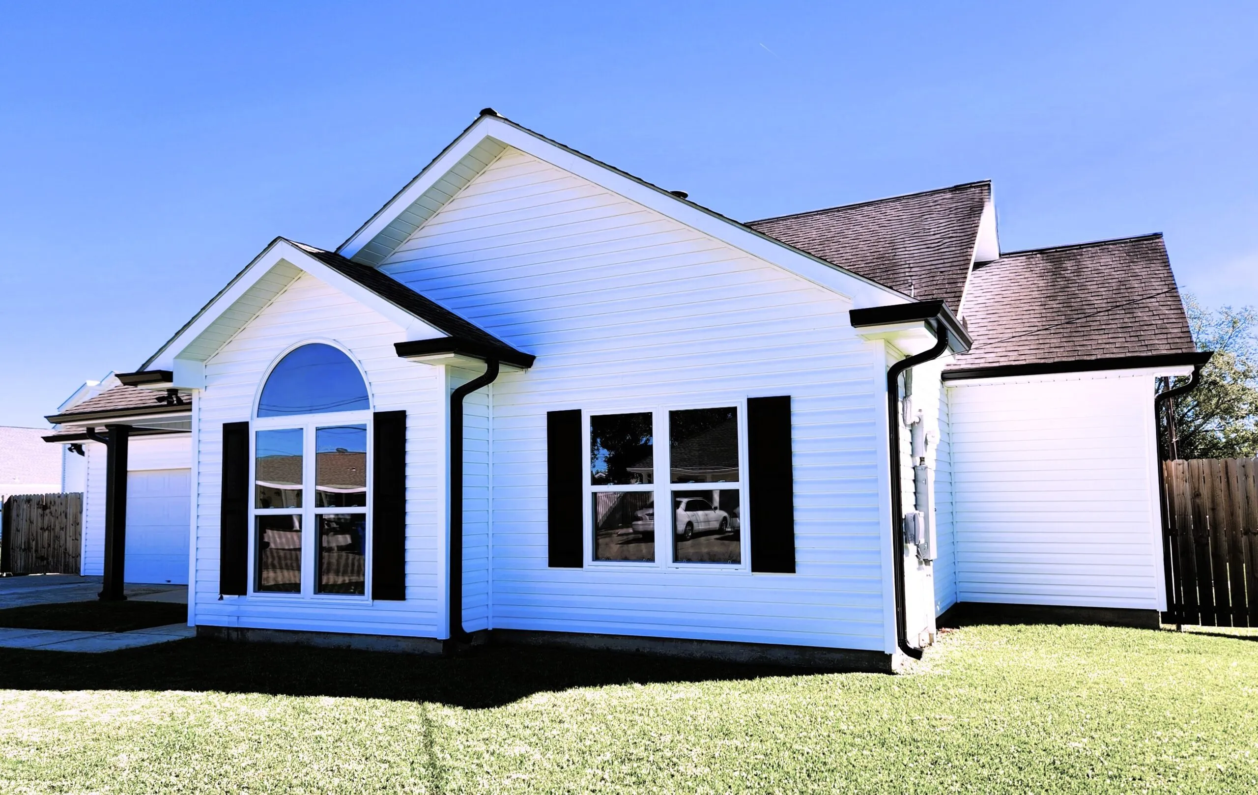 Newly renovated home exterior showcasing seamless aluminum gutters, white siding, black shutters, and a modern architectural design, emphasizing quality home improvement services.