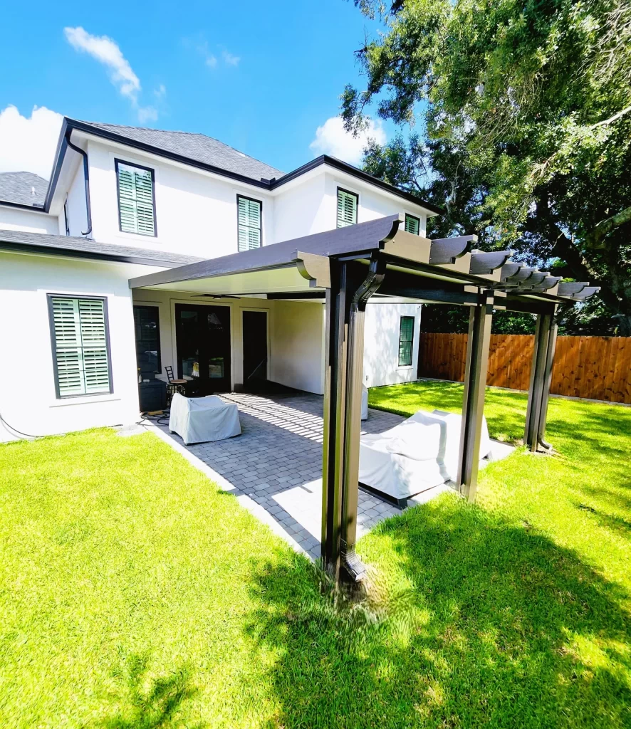 Patio cover featuring insulated laminated roof panels, providing shade and weather protection, attached to a modern home with green grass and a paved area.