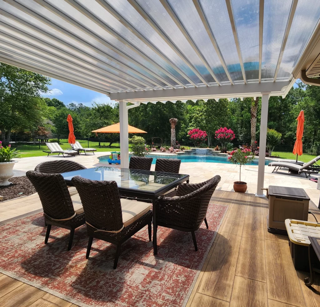 Patio cover featuring insulated laminated roof panels over a stylish outdoor dining set, with a pool and landscaped garden in the background, showcasing durability and versatility for outdoor living spaces.