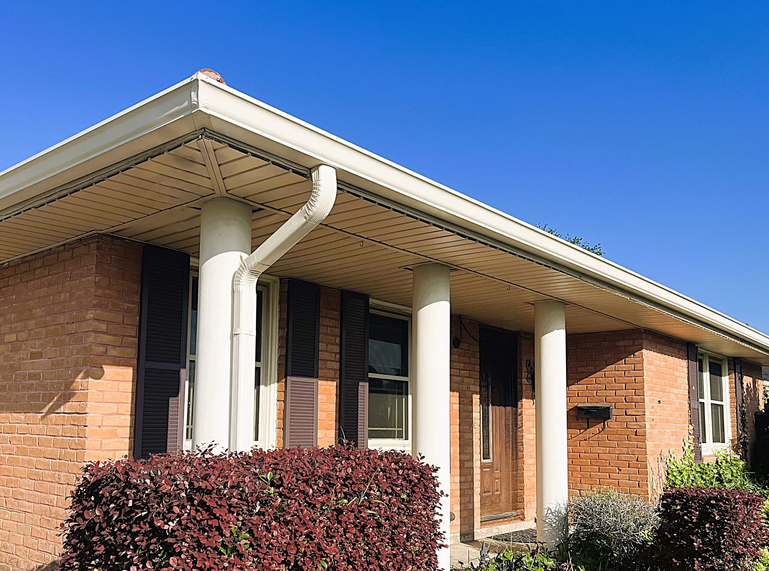 Seamless aluminum gutters installed on a brick home, showcasing professional exterior design and maintenance-free features, with vibrant landscaping and a clear blue sky.