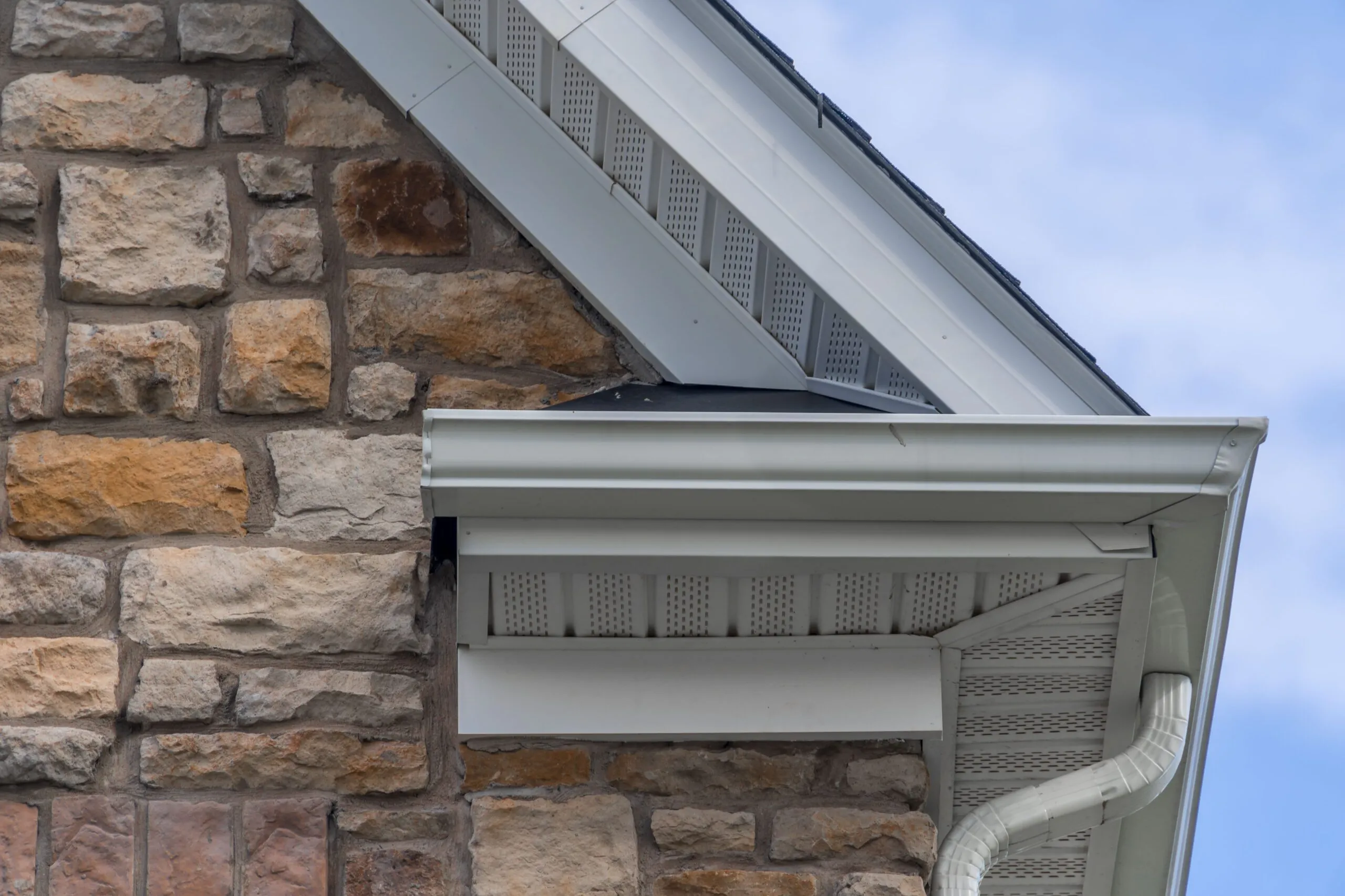 Seamless aluminum gutter installation on a stone home exterior, showcasing precision craftsmanship and effective water diversion features.