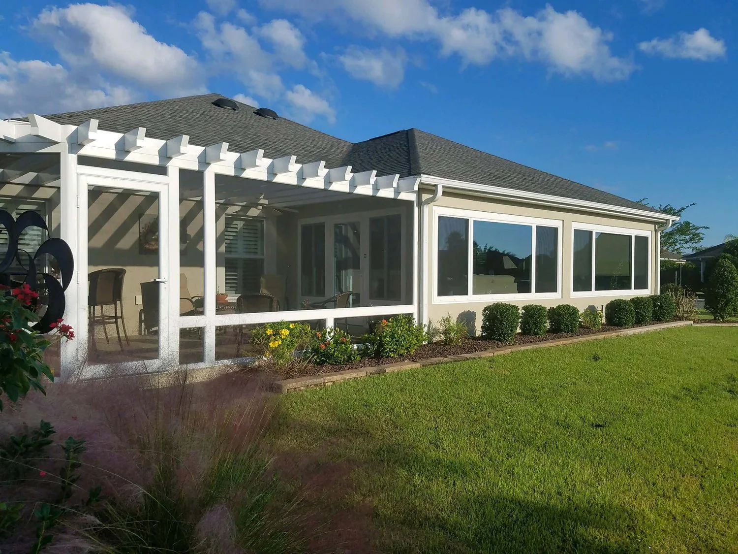 Sunroom addition with large windows, white frame, and shaded patio area, surrounded by landscaped garden in a sunny outdoor setting, illustrating ideal space for enjoying New Orleans weather.