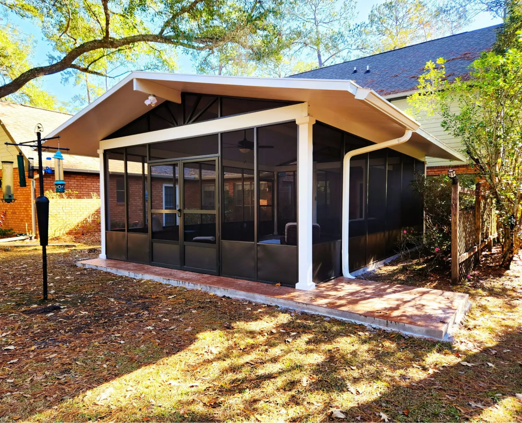 Screened-in patio with a modern design, featuring a peaked roof, large windows, and a spacious outdoor area, surrounded by trees and grass, ideal for outdoor living in Metairie.