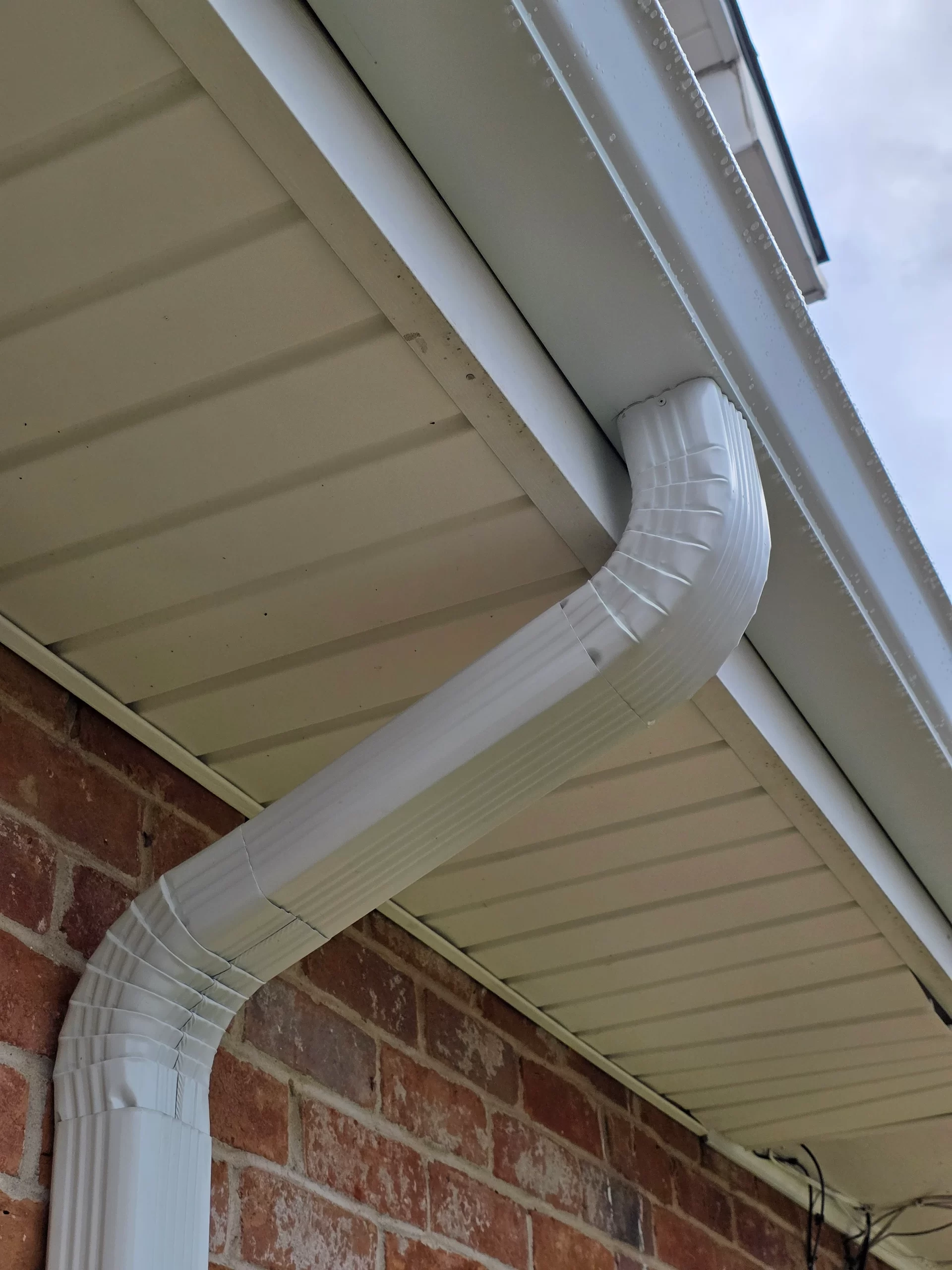 Seamless white gutter system installed on a brick home, showcasing a clean and efficient water drainage solution, relevant to home improvement in Louisiana's rainy climate.
