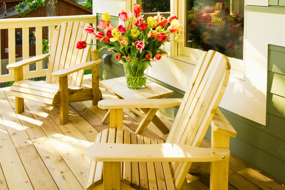 Wooden adirondack chairs on a sunny porch with a vibrant bouquet of tulips on a side table, illustrating an inviting outdoor living space for relaxation and gatherings.