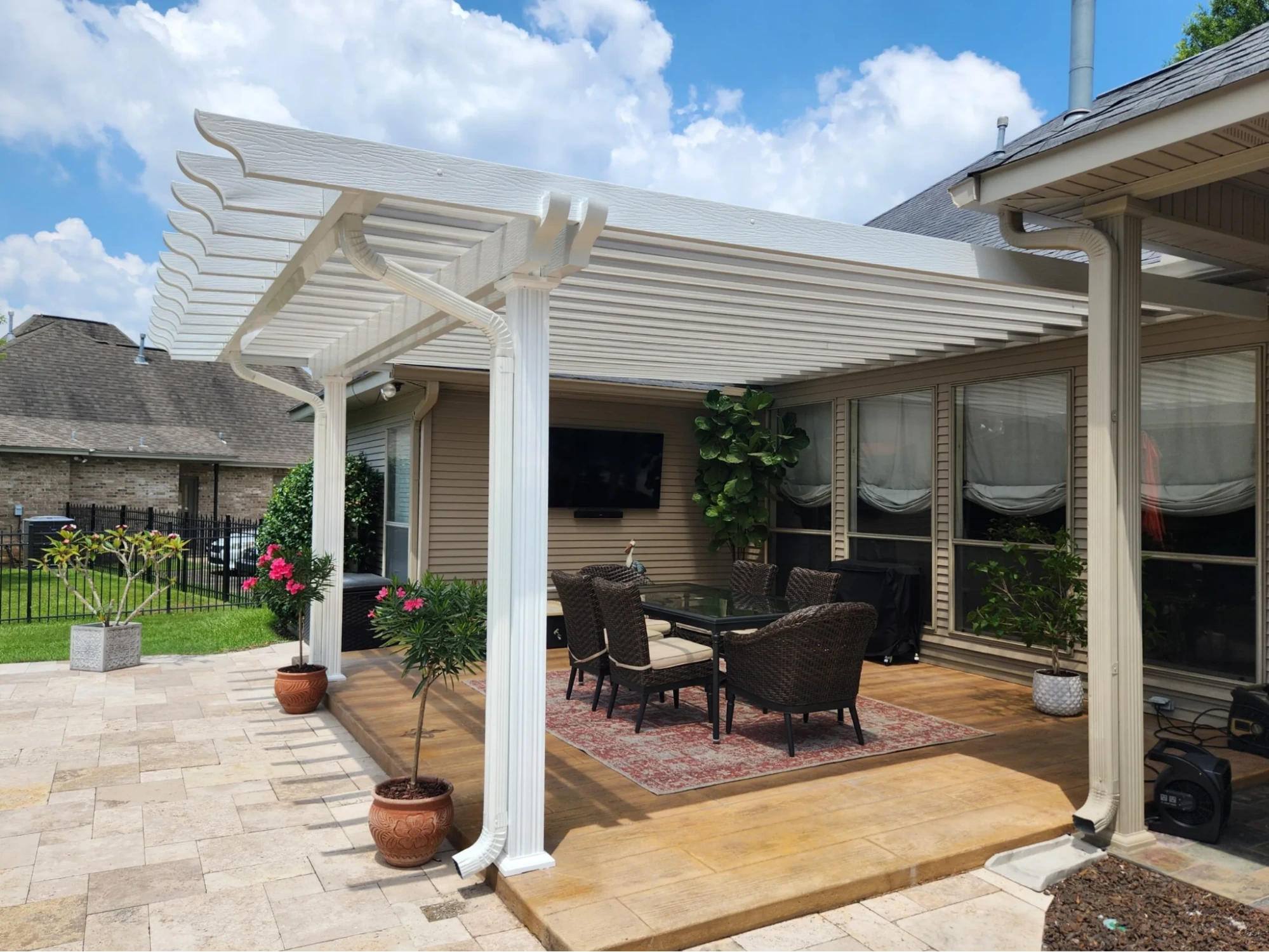 Non-insulated patio cover with white slatted roof, providing shade over outdoor seating area with wicker furniture and potted plants, enhancing backyard comfort and aesthetics.