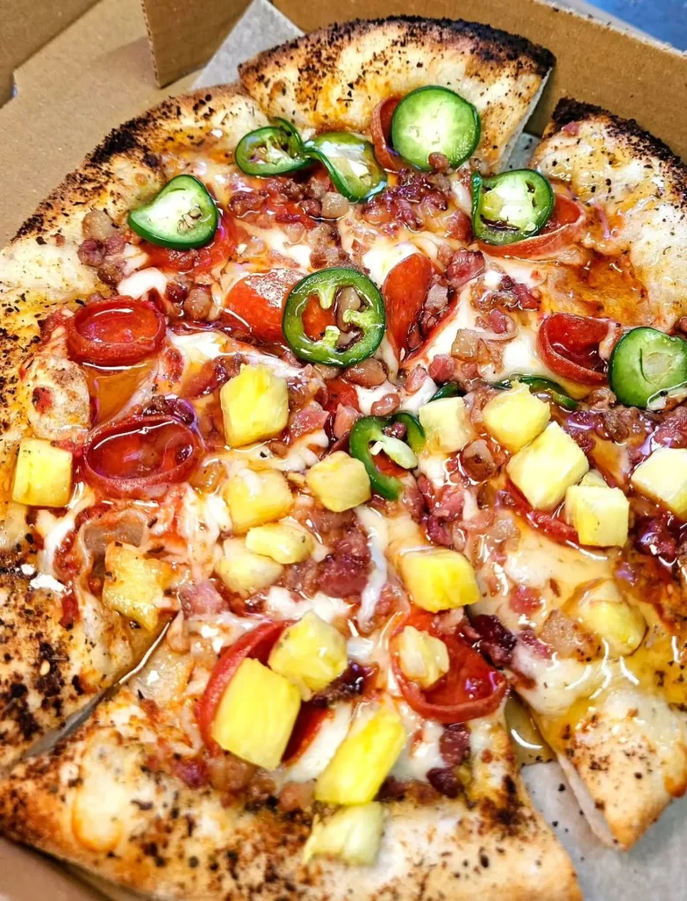 Southern Fired Foods, Grovetown, GA: overhead close-up of a loaded pizza in a to-go box, topped with pepperoni, bacon bits, sliced jalapenos, diced pineapple, and melted cheese, charred crust edges