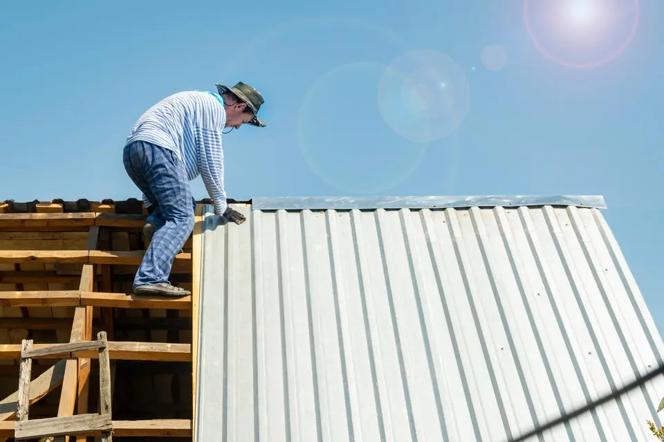 types of metal roofs-man installing white corrugated metal roof on a house