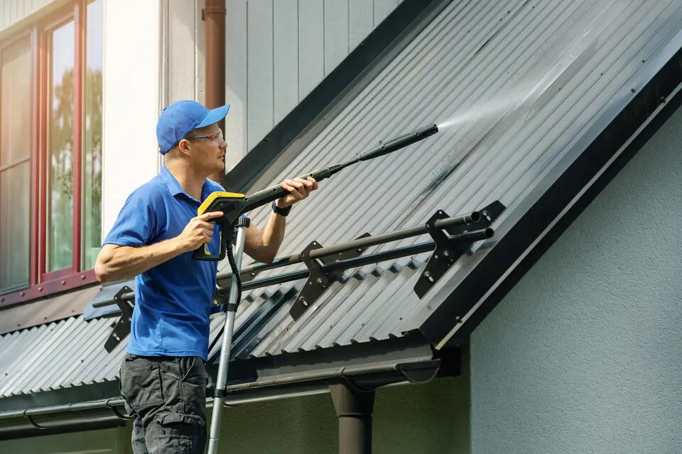 how much to pressure wash a 2,000 sq ft house-man standing on a ladder leaning on a roof pressure washing the metal roof
