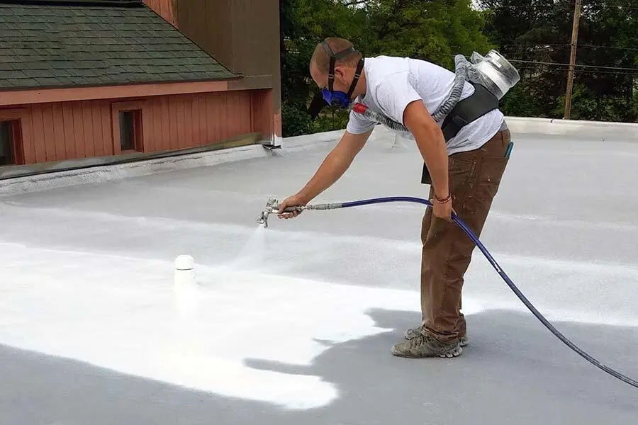spray foam roofing-man wearing face mask installing spray foam on flat roof