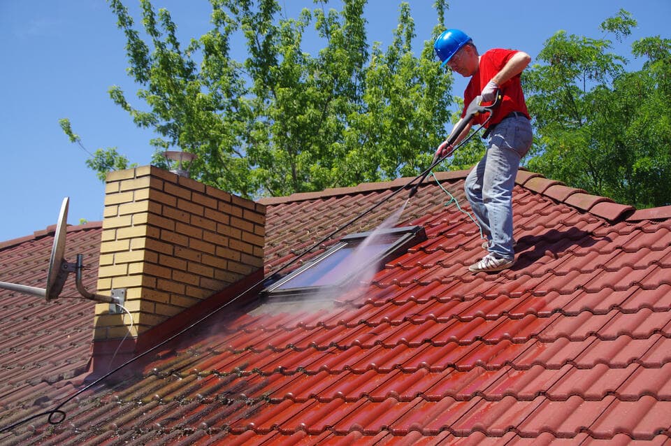 how much to pressure wash a 2,000 sq ft house-man wearing a safety hat pressure washing a red tile roof