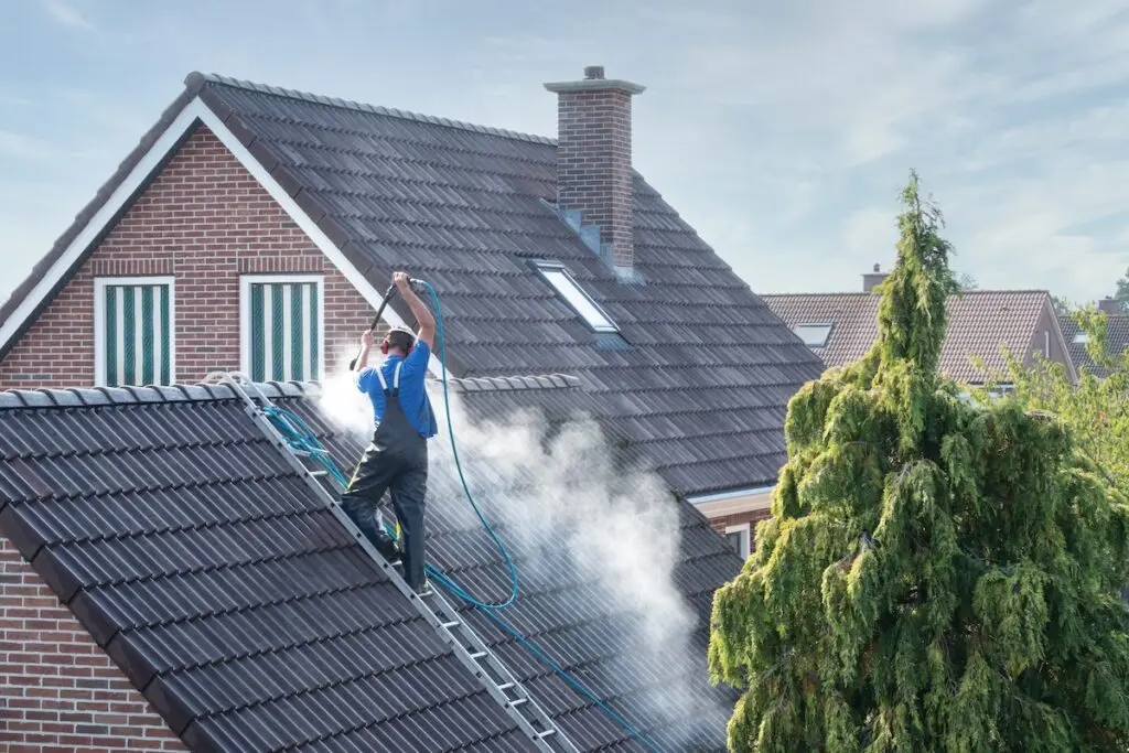Cleaner with pressure washer at roof of house cleaning the roof tiles, removing moss and weed terracotta roof tile cleaning