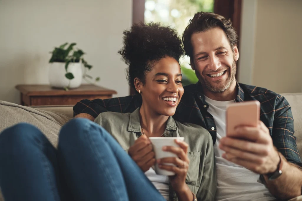 young couple smiling and looking at phone on the couch
