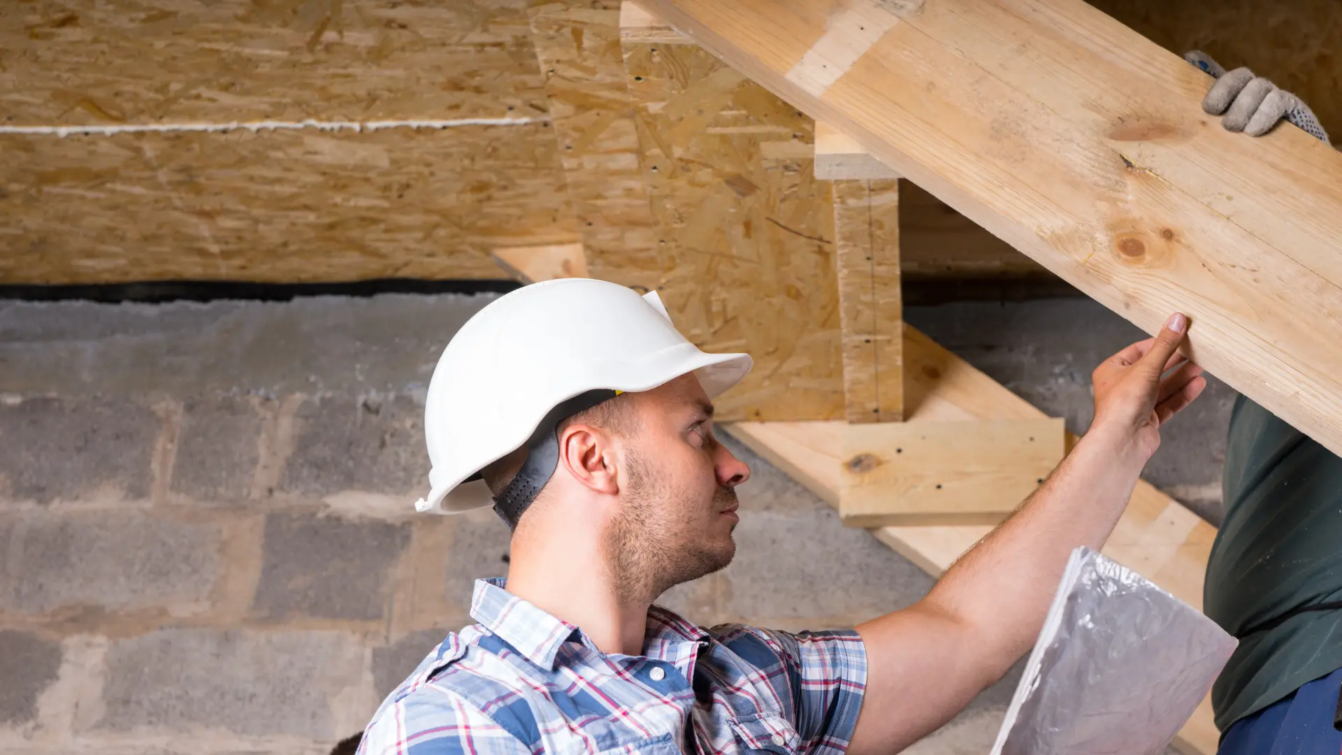 Construction worker in a hard hat assessing wooden beams during a structural inspection, emphasizing the importance of thorough evaluations in home maintenance.