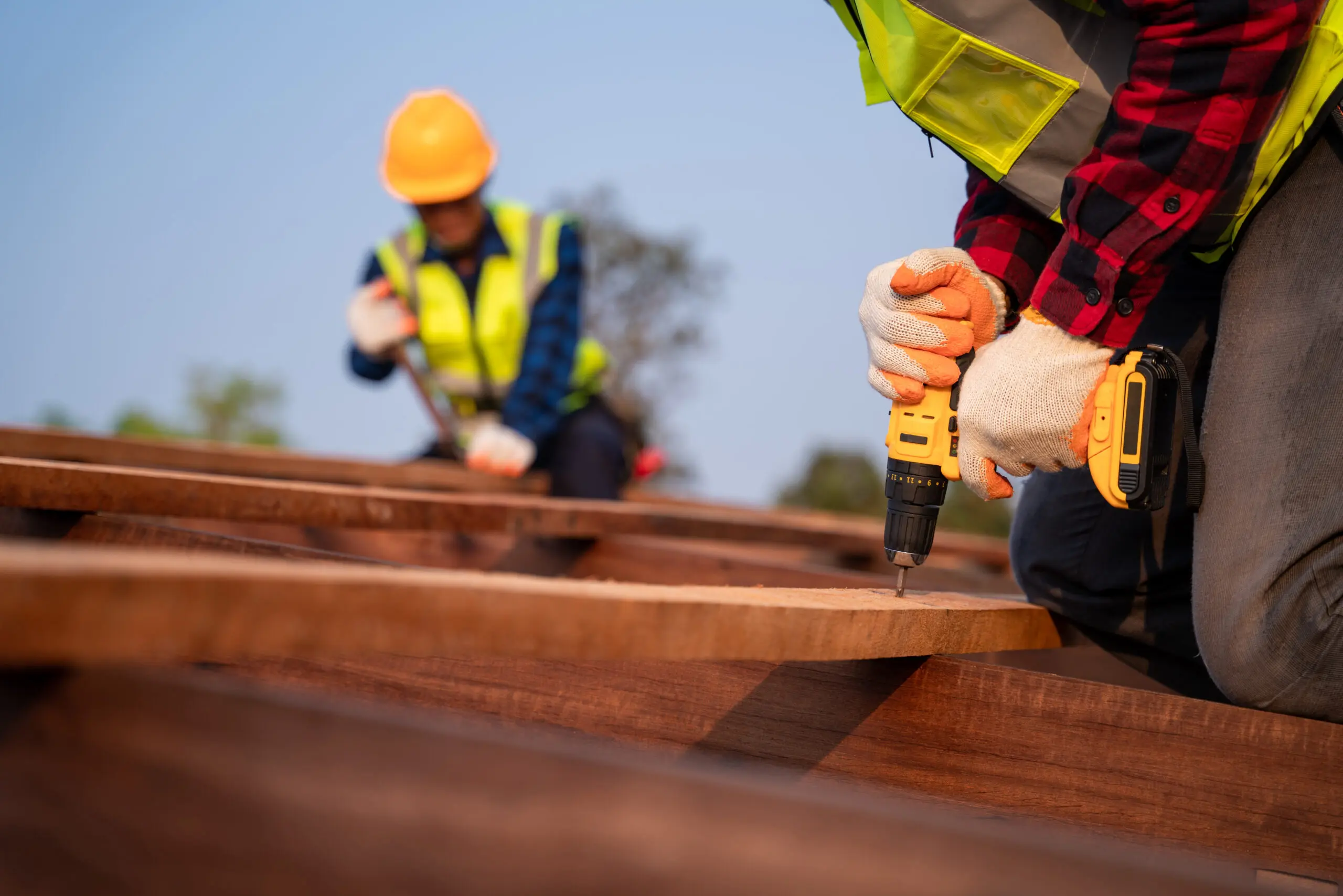 Roofers working on a construction site, using power tools to install roofing materials, showcasing safety gear and teamwork in a residential roofing project.