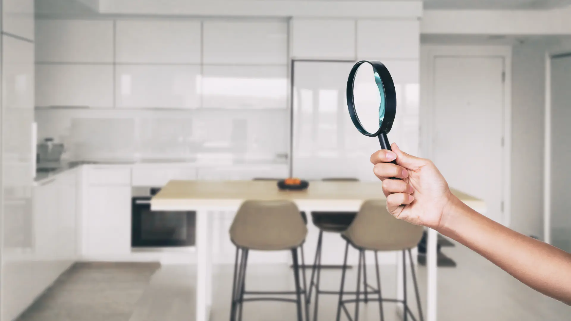 Hand holding a magnifying glass in a modern kitchen, emphasizing the importance of thorough interior inspections for identifying potential hazards and issues in home evaluations.
