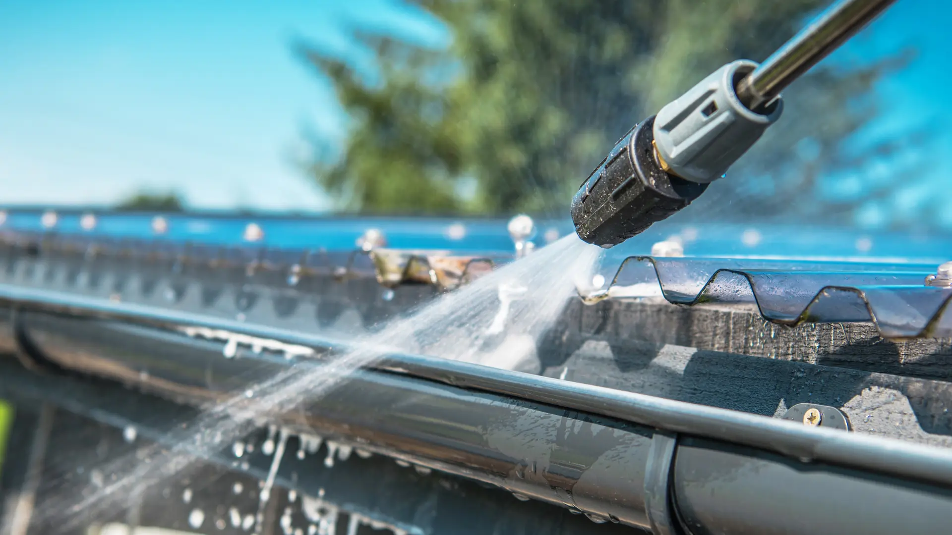 Power washer cleaning residential gutters to prevent water damage and maintain home exterior.