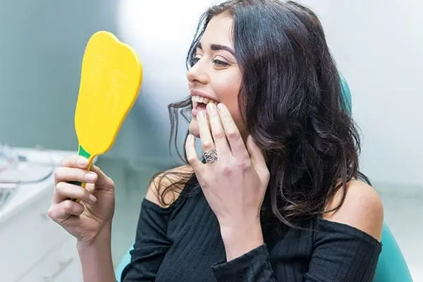 Woman checking her teeth in the mirror after a comprehensive dental exam in Greenwood Village