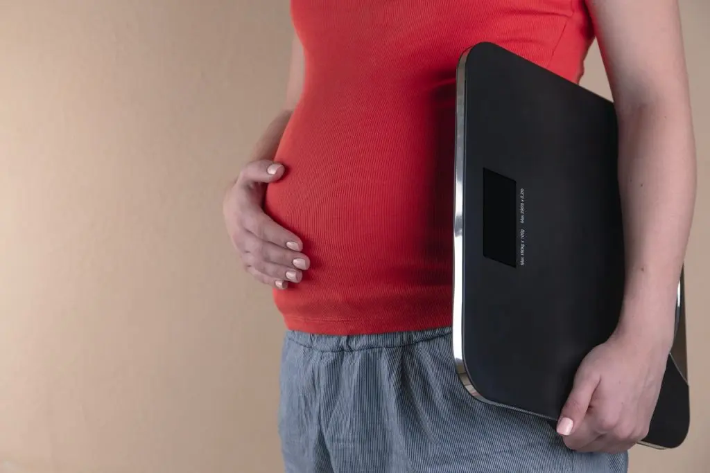 person holding their stomach and a weighing scale