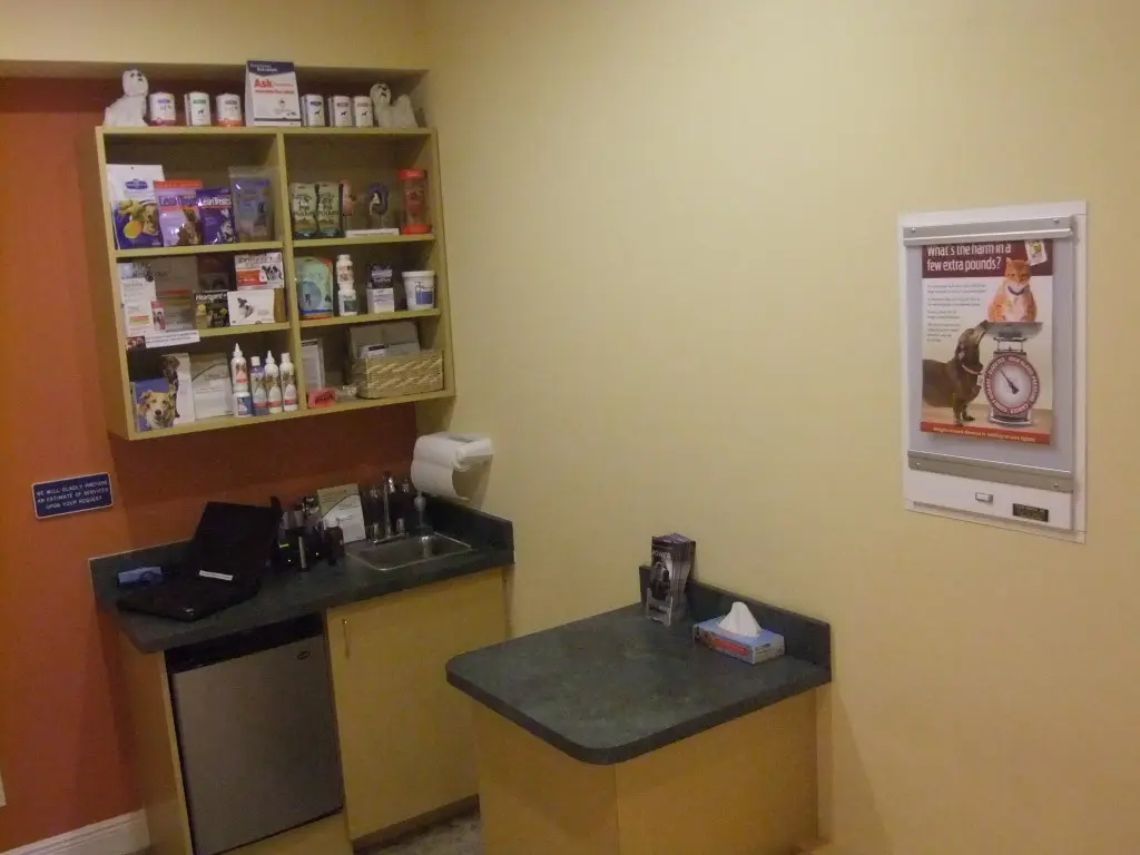 A veterinary exam and prep room at Cross Creek Animal Medical Centre in Tampa, FL features cabinetry, a mini-fridge, sink, and stocked shelving.