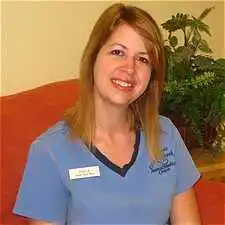 Paula Hendrickson, a Senior Technician at Cross Creek Animal Medical Centre, smiles in blue scrubs against a red couch.