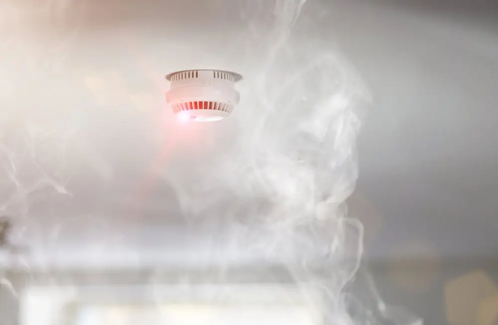 Smoke alarm on ceiling with smoke around it