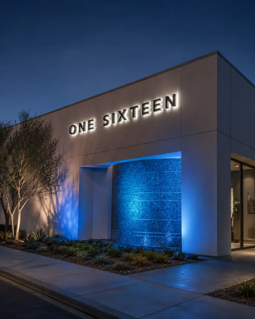 Modern building exterior at night with an illuminated 'ONE SIXTEEN' sign and blue accent lighting on the entrance wall.