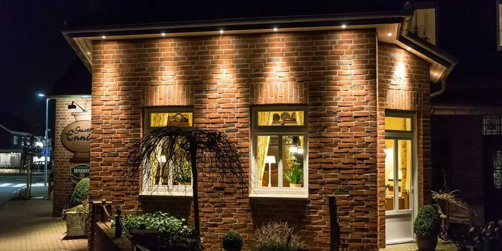 Bright exterior lights illuminate a red brick house facade at night, demonstrating tips from a comprehensive exterior house uplighting guide.