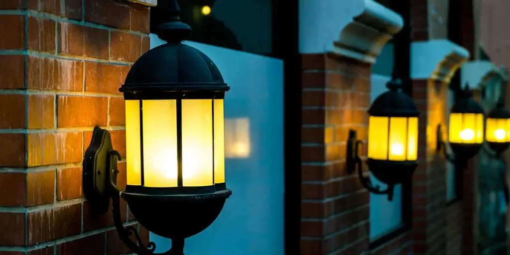 Warm yellow outdoor lantern lights glowing on a brick wall, providing effective bug resistant illumination for home exterior patio spaces.