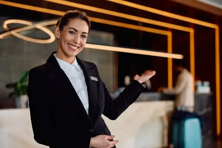 Happy concierge welcoming guests in a hotel and looking at camera.