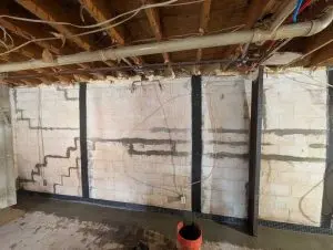 Interior French drain and carbon fiber wall strap installation completed in a lake house basement in Erie, PA by ARK Basement Services.