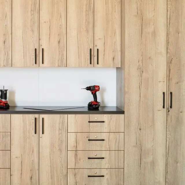 Professional light wood garage storage cabinets installed with black handles and tools.