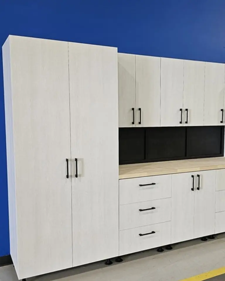 Higgins Distribution white garage storage cabinets with black hardware installed against a blue wall.