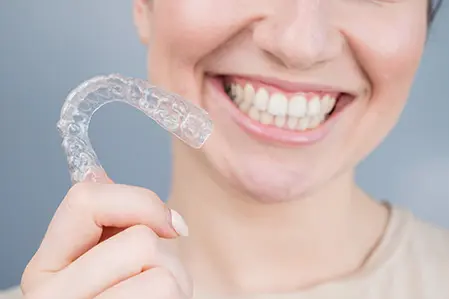 Woman smiling while holding her Invisalign braces