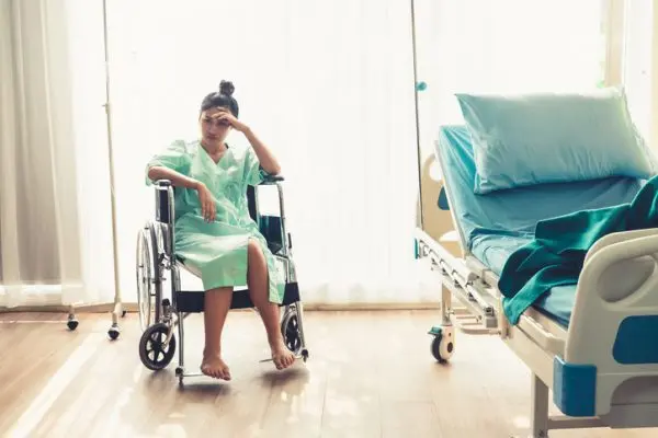 Serious patient sitting on wheelchair in hospital ward. Bad health result made the patient unhappy. Medical malpractice concept.
