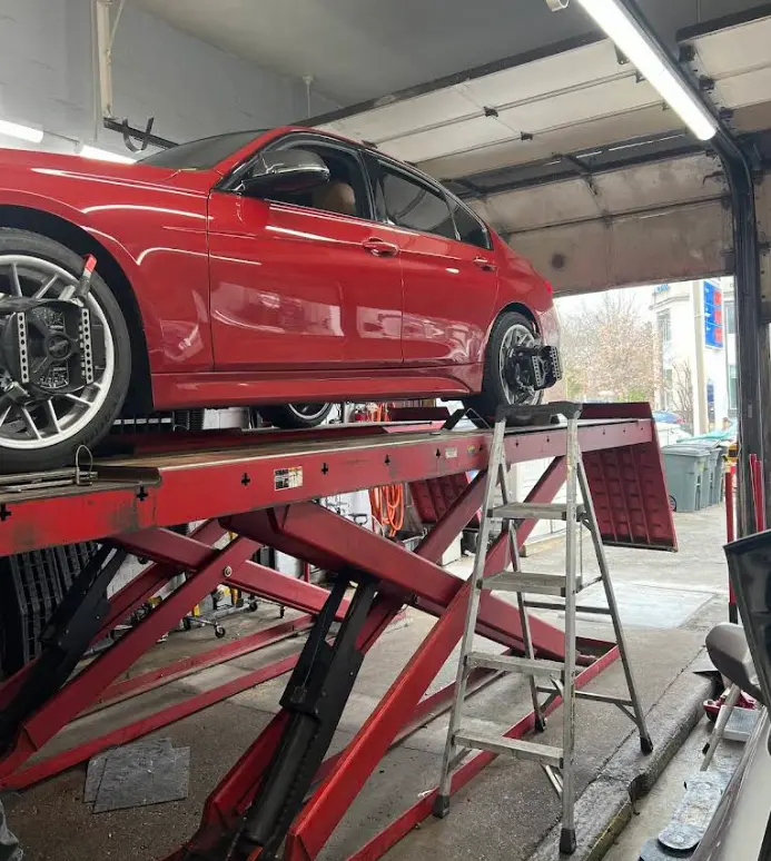 Red sedan on a scissor lift inside an auto repair shop bay, no people visible