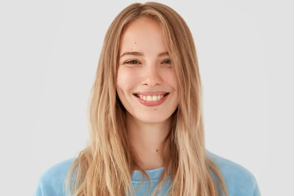 Woman with long dark blond hair smiling and showing her teeth after dental services from a cosmetic dentist in Midland