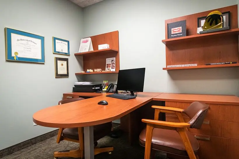 Private office space with a wooden desk, black office chair, and shelving inside Knight Dental Care in Midland, MI
